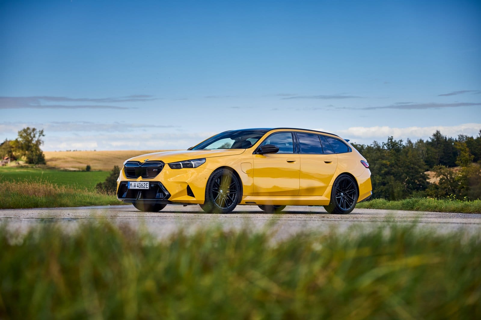 Front-side view of the yellow 2025 BMW M5 Touring Plug-in Hybrid parked beside a countryside road