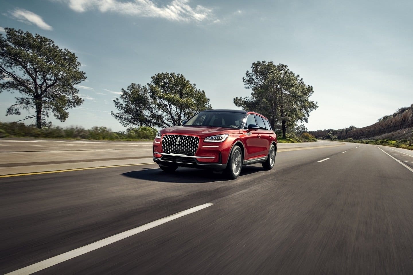 Front view of red Lincoln Corsair Grand Touring plug-in hybrid driving on a highway with trees in background