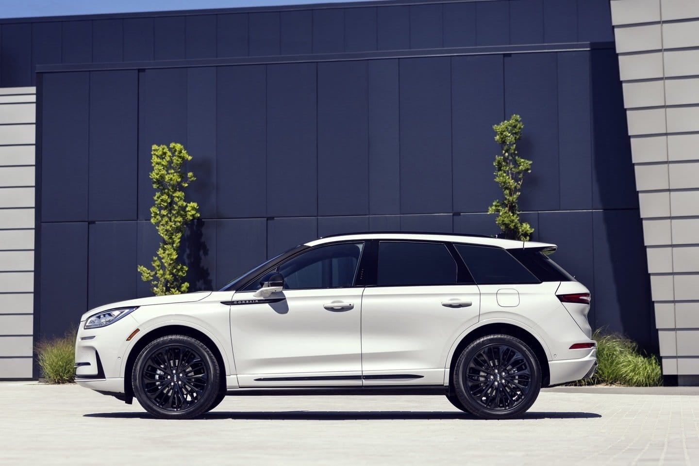 White Lincoln Corsair Grand Touring plug-in hybrid SUV viewed from the side, parked in front of a modern building