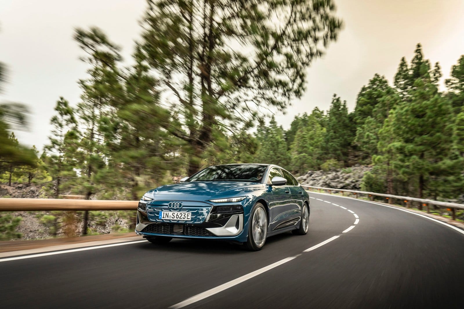 Audi S6 e-tron electric vehicle driving on a curving road through a forest with motion blur in the background.