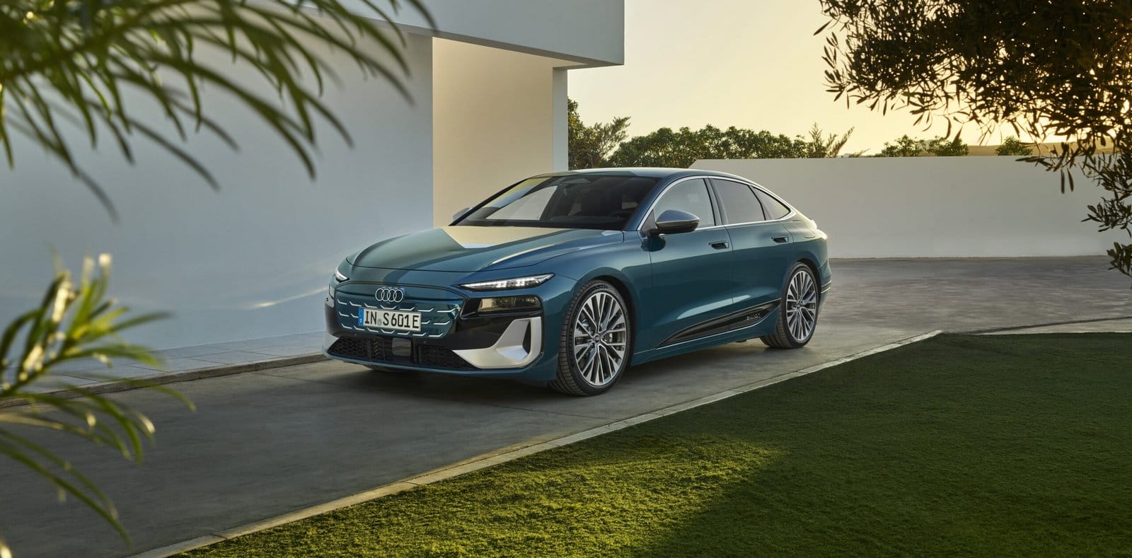 Front view of Audi S6 e-tron electric vehicle parked on a driveway near a modern white building and greenery.