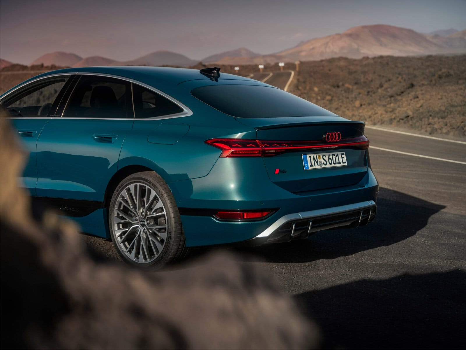 Rear side view of Audi S6 e-tron electric vehicle highlighting tail lights, sportback design, and alloy wheels on a mountain road.