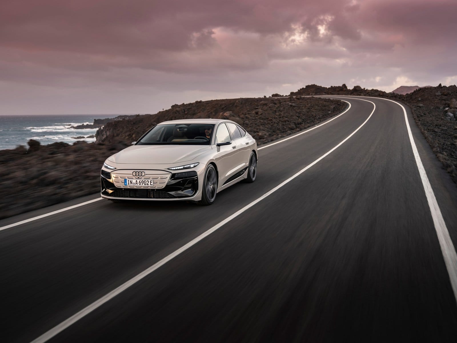 2025 Audi A6 e-tron electric vehicle driving on a winding coastal road at sunset