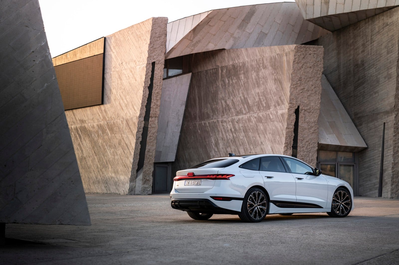 Rear side view of the 2025 Audi A6 e-tron electric vehicle parked in front of modern concrete architecture