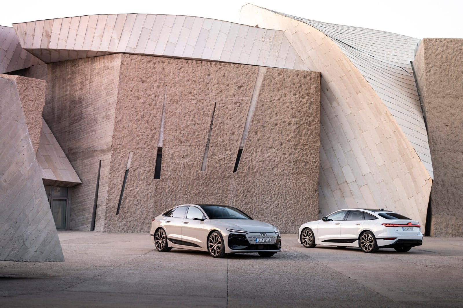 Two Audi A6 e-tron electric vehicles parked near modern stone architecture, showing front and rear angles.