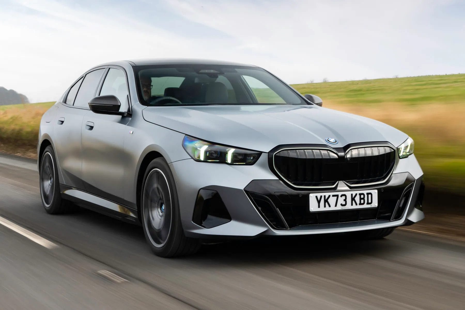 BMW 550e xDrive electric vehicle photographed from the front while driving on a rural road