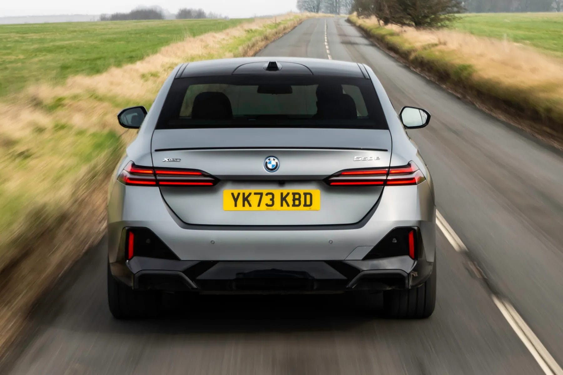 BMW 550e xDrive electric vehicle photographed from the rear while driving on a country road