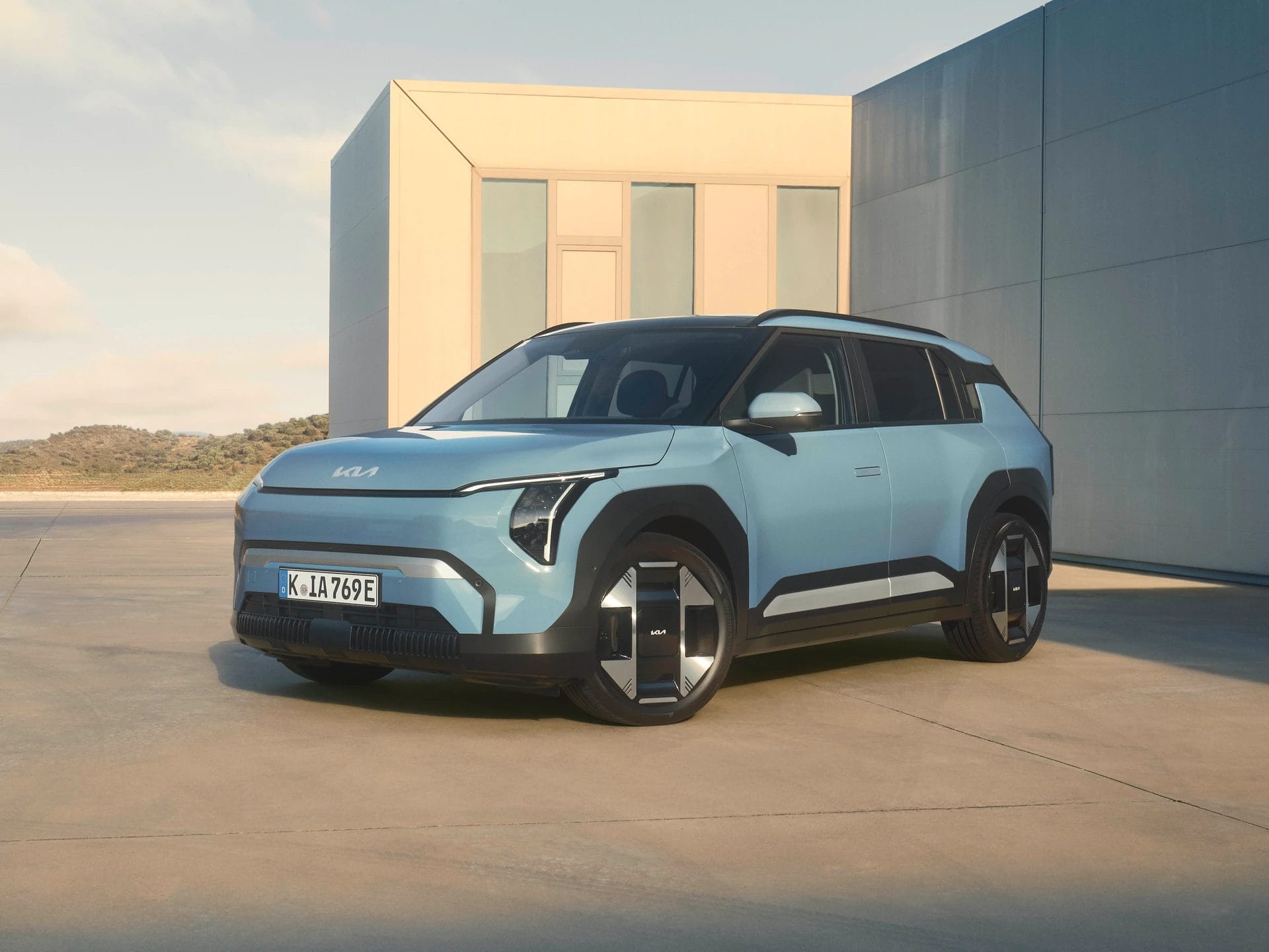 Blue Kia EV3 electric vehicle front angle view parked near modern architecture
