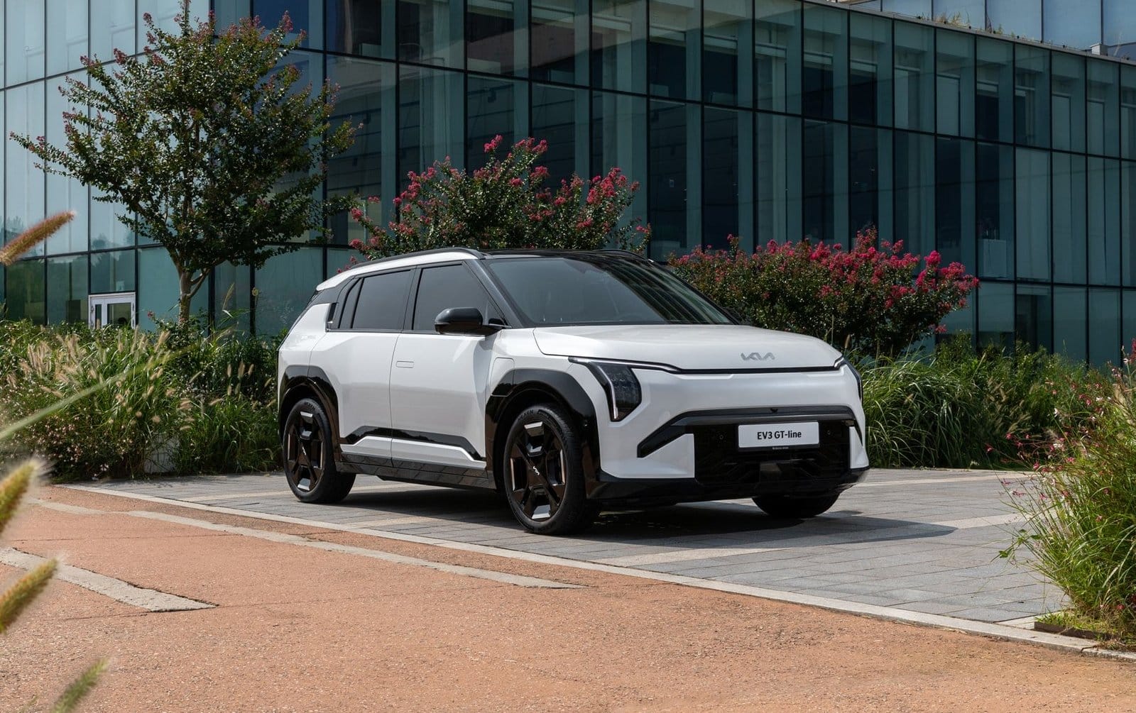 Front three-quarter view of Kia EV3 electric vehicle parked beside modern glass building