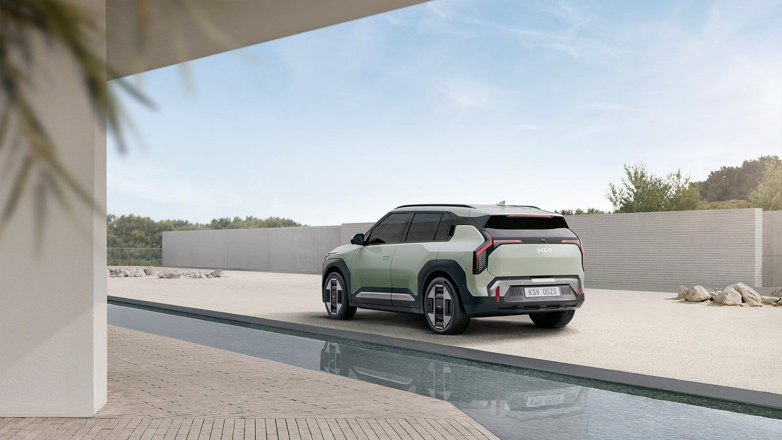Rear angle of Kia EV3 electric vehicle parked beside minimalist building with water feature