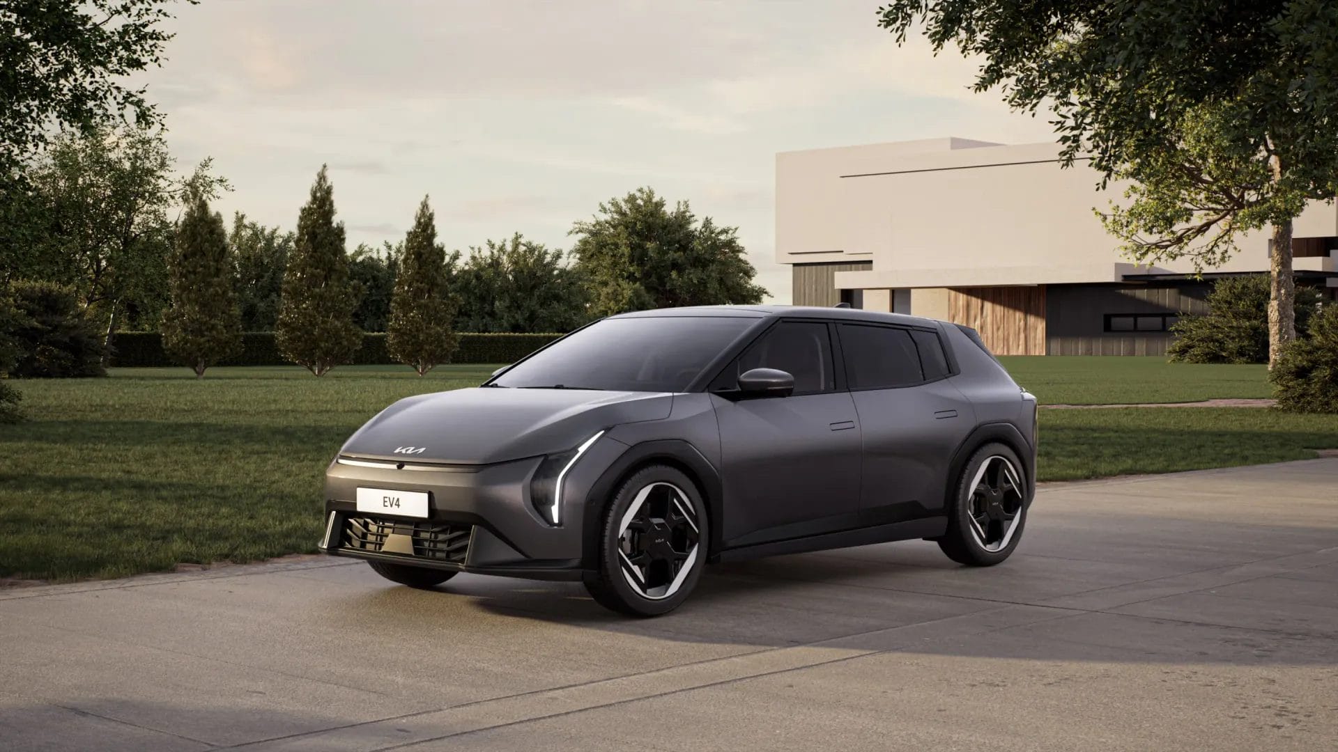 Front angle photograph of Kia EV4 electric vehicle parked on a driveway with trees and a house in the background