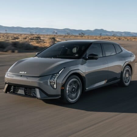 Front view of Kia EV4 electric vehicle driving on a desert highway with mountains in the background