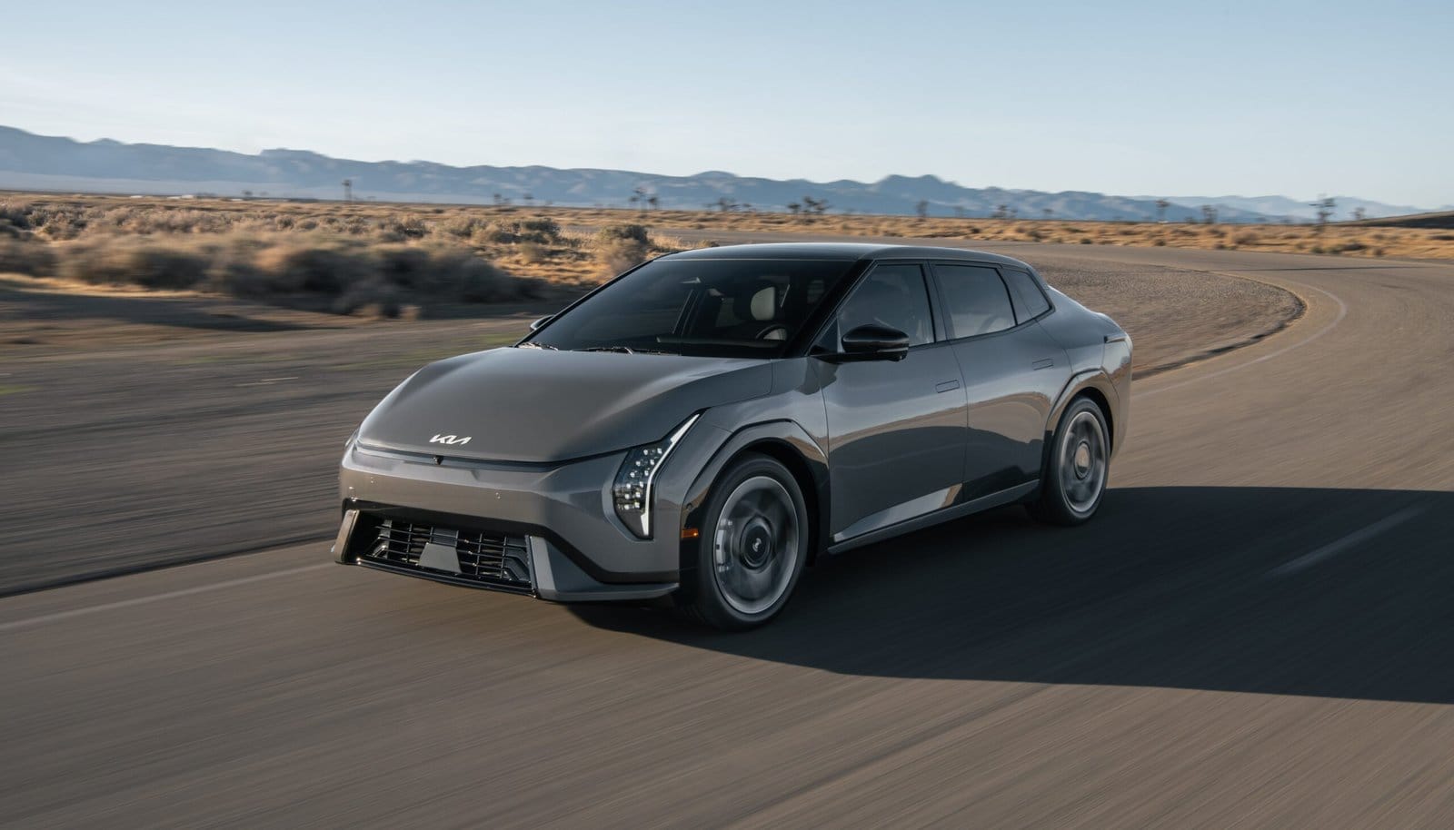 Front view of Kia EV4 electric vehicle driving on a desert highway with mountains in the background
