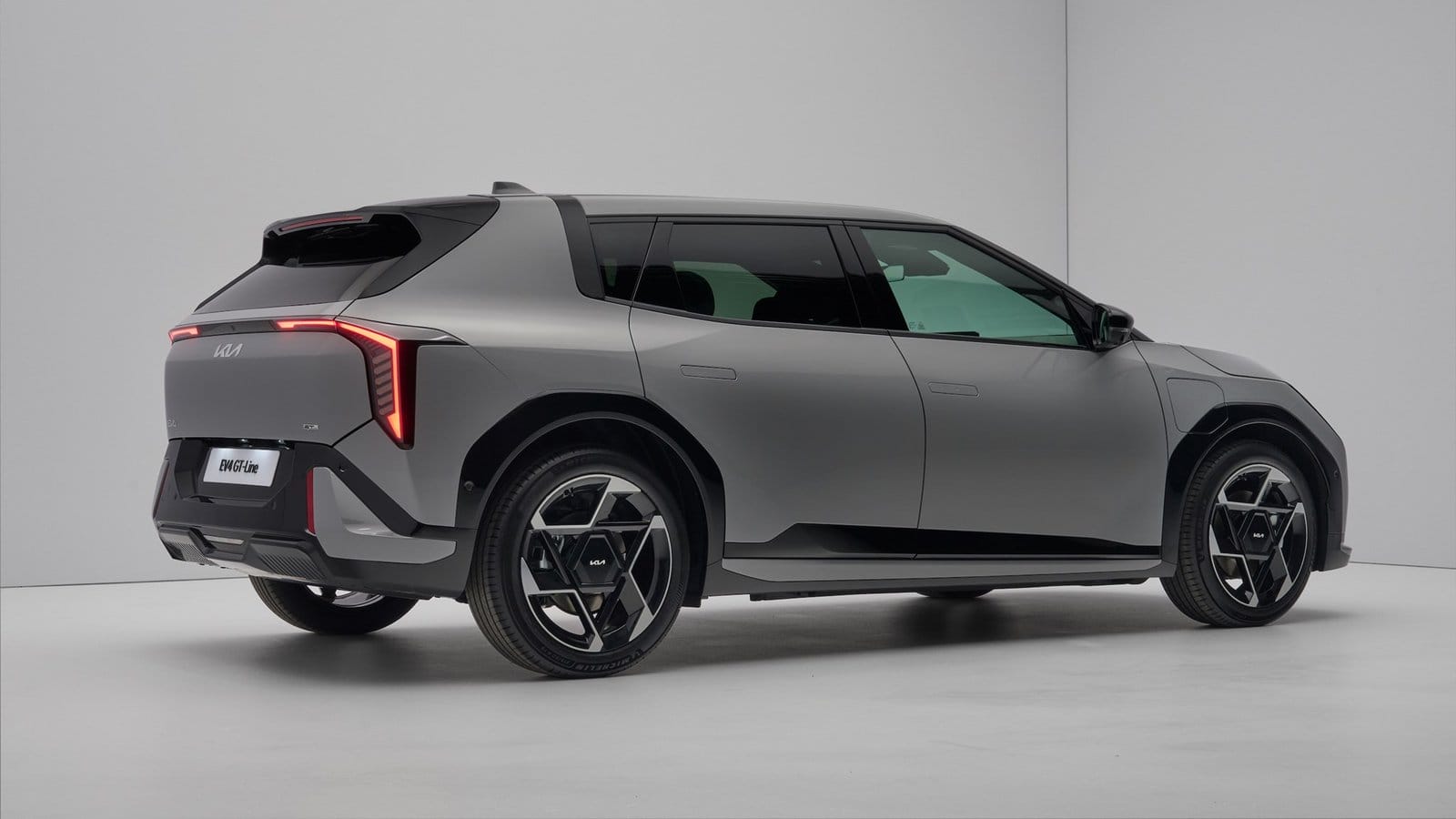 Rear side angle of Kia EV4 electric vehicle GT-Line showing illuminated tail lights and alloy wheels