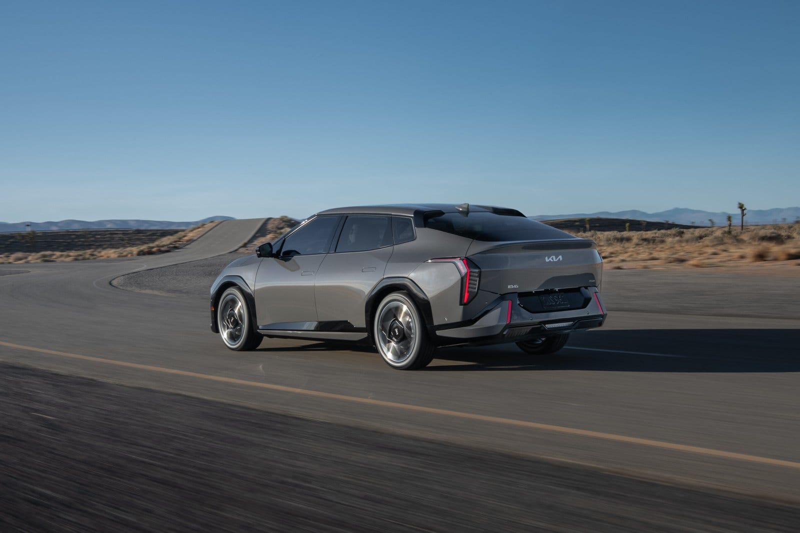 Rear view of Kia EV4 electric vehicle driving on a desert highway with illuminated tail lights
