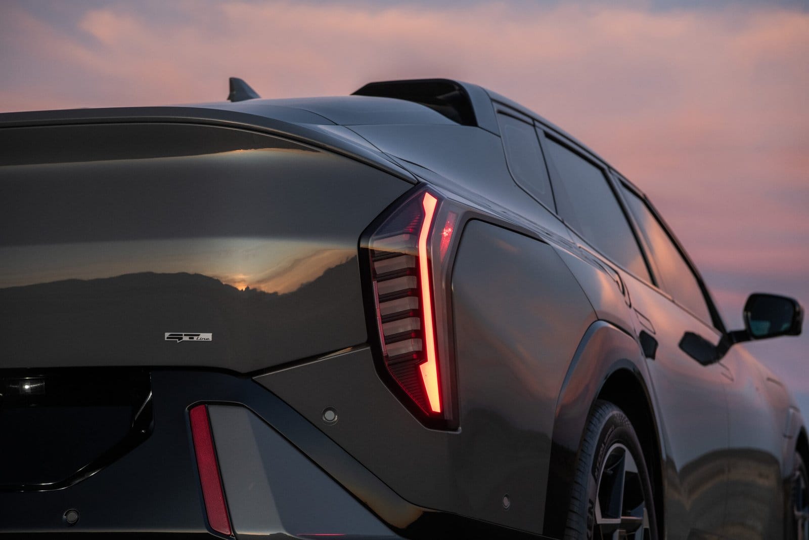 Rear close-up of Kia EV4 electric vehicle with illuminated tail lights and GT-Line badge at sunset